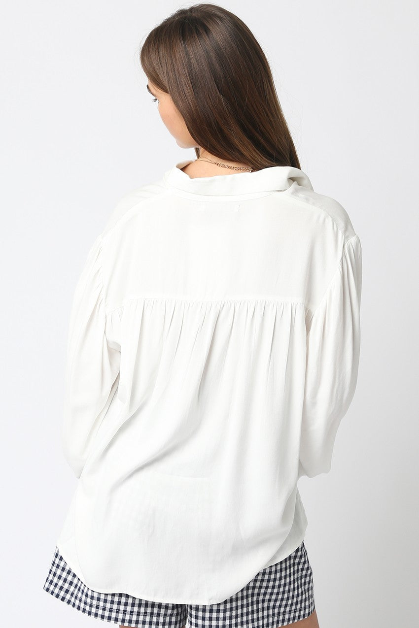 Person wearing a white blouse with long sleeves on a plain background