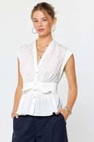 Woman wearing a white sleeveless blouse with a belt and navy pants on a white background