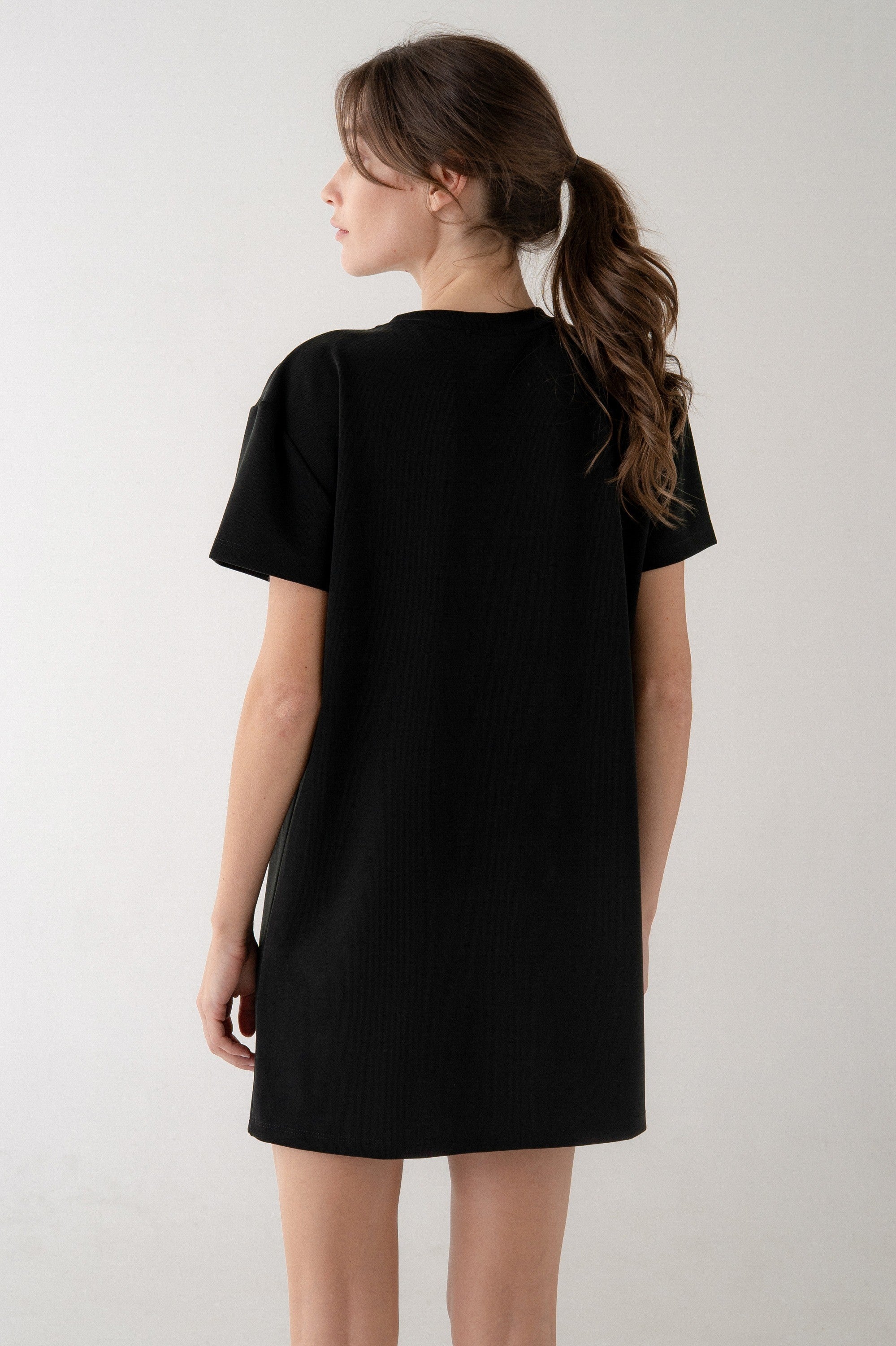 Person wearing a black t-shirt dress against a white background