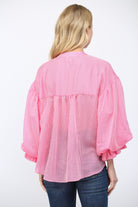 Person wearing a pink checkered blouse with ruffled sleeves on a white background