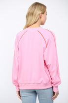 Person wearing a pink sweatshirt with orange accents on a white background