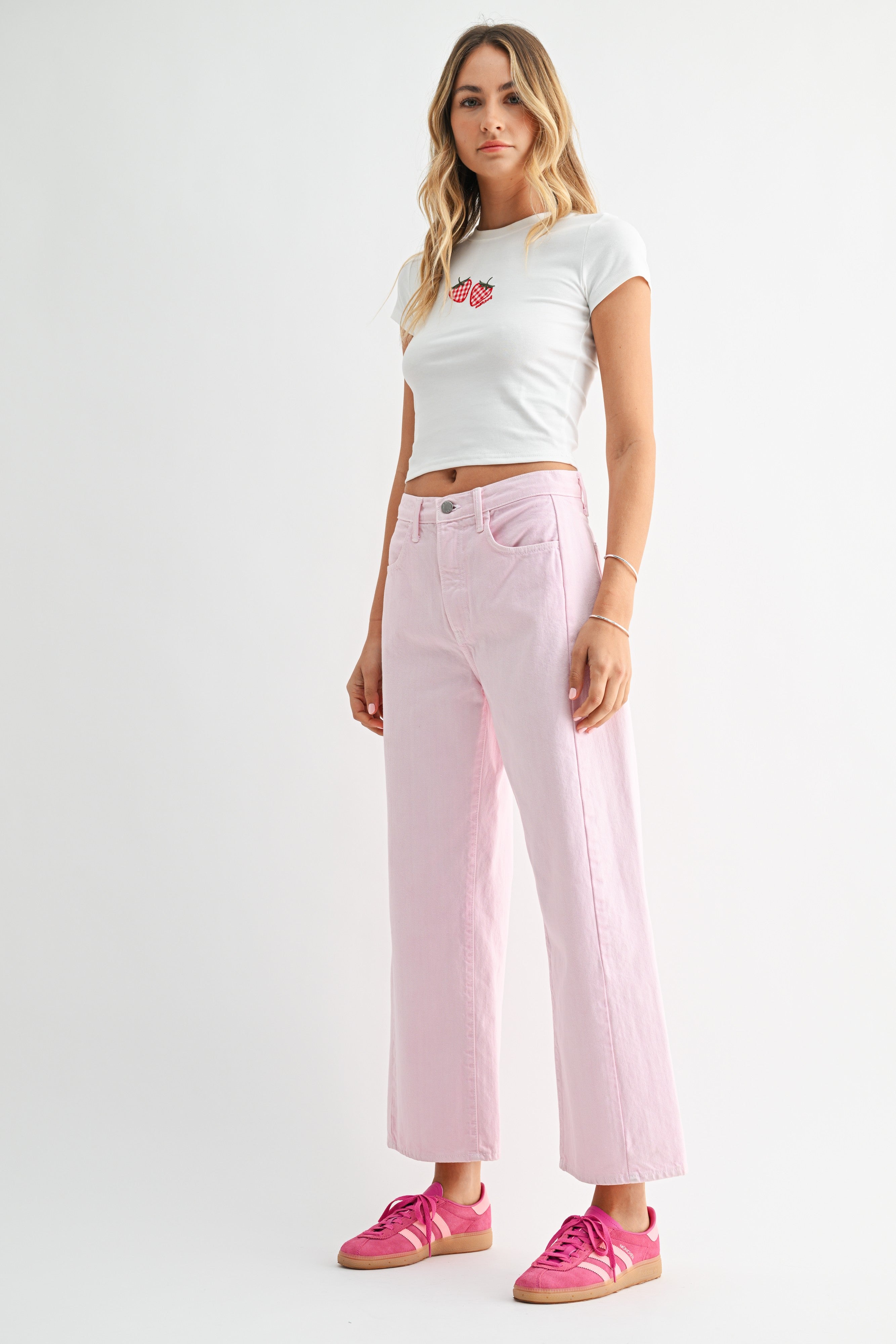 Woman wearing a white crop top and pink jeans on a white background