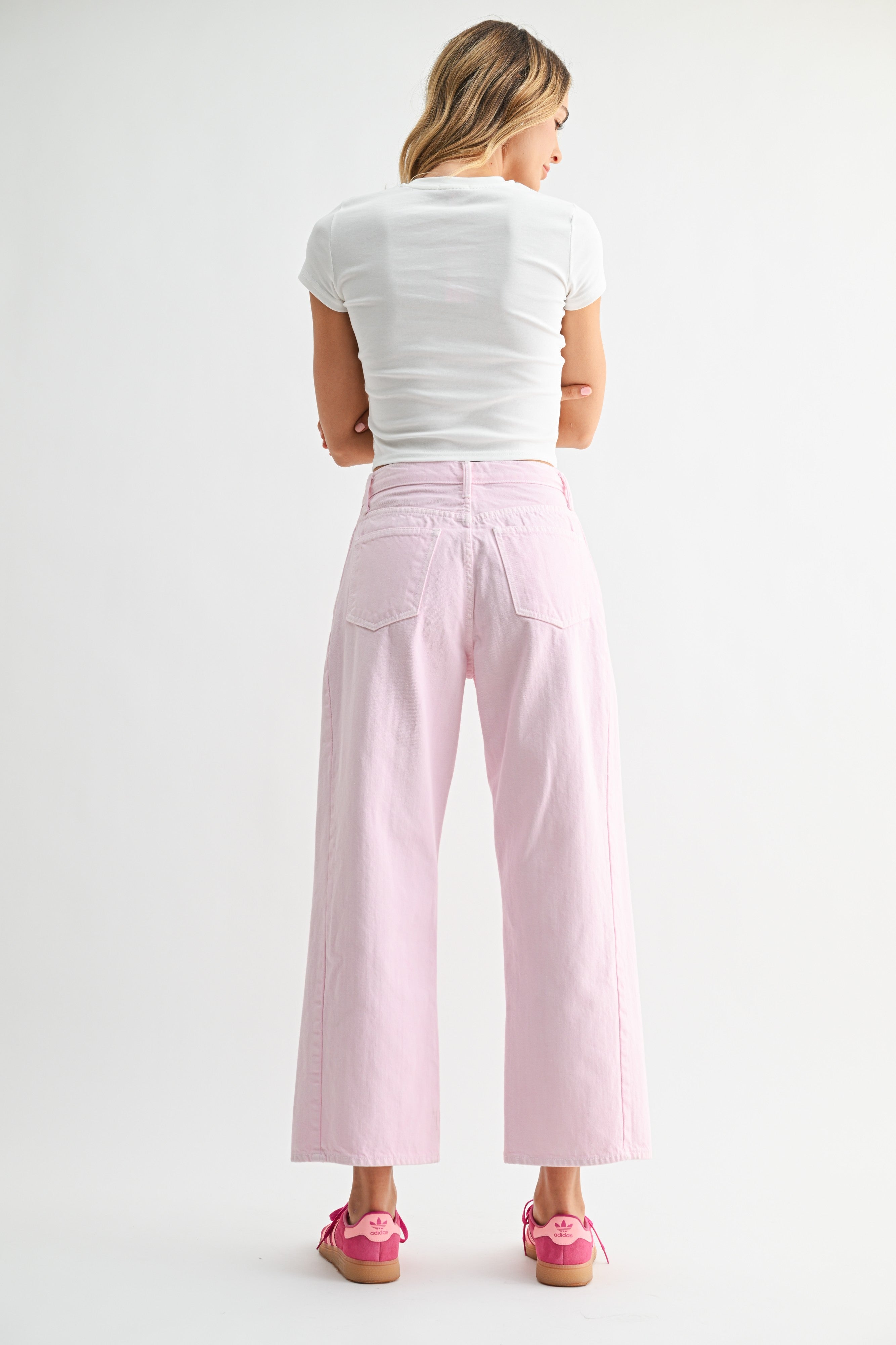 Woman wearing light pink pants and a white top on a plain background