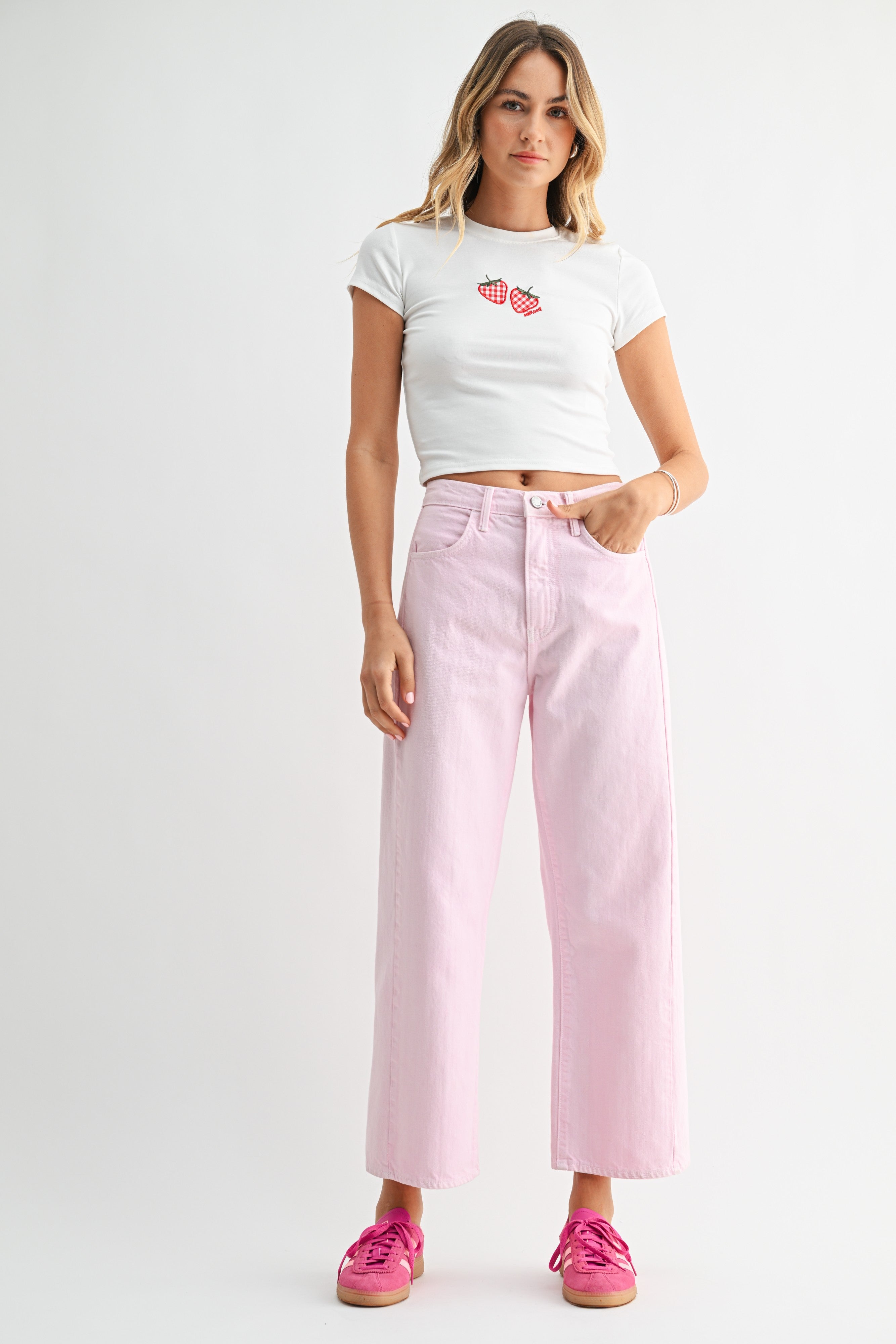 Woman wearing a white crop top with red graphics and pink high-waisted jeans on a white background