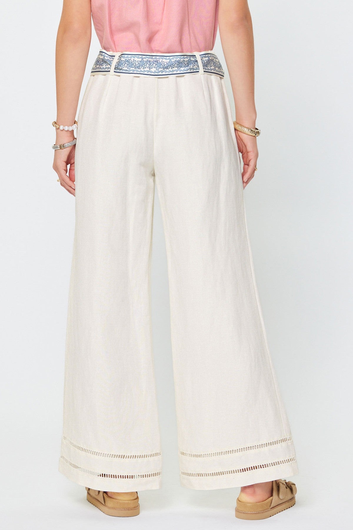 Person wearing white wide-leg pants with decorative trim on a white background