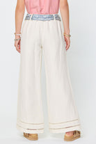 Person wearing white wide-leg pants with decorative trim on a white background