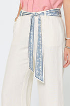 White pants with a blue patterned belt on a plain background