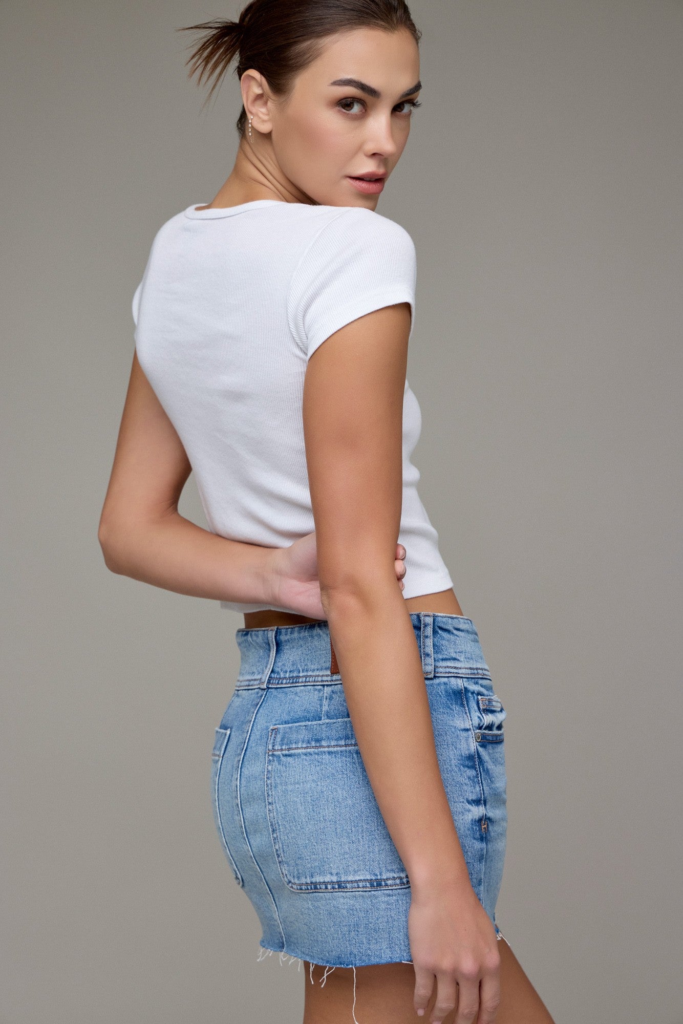 Woman wearing a white t-shirt and denim shorts against a gray background