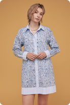 Woman wearing a blue floral dress over a white shirt on a mustard yellow background