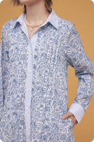 Person wearing a blue floral dress over a striped shirt against a mustard yellow background