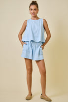 Woman wearing a light blue sleeveless top and shorts set on a beige background