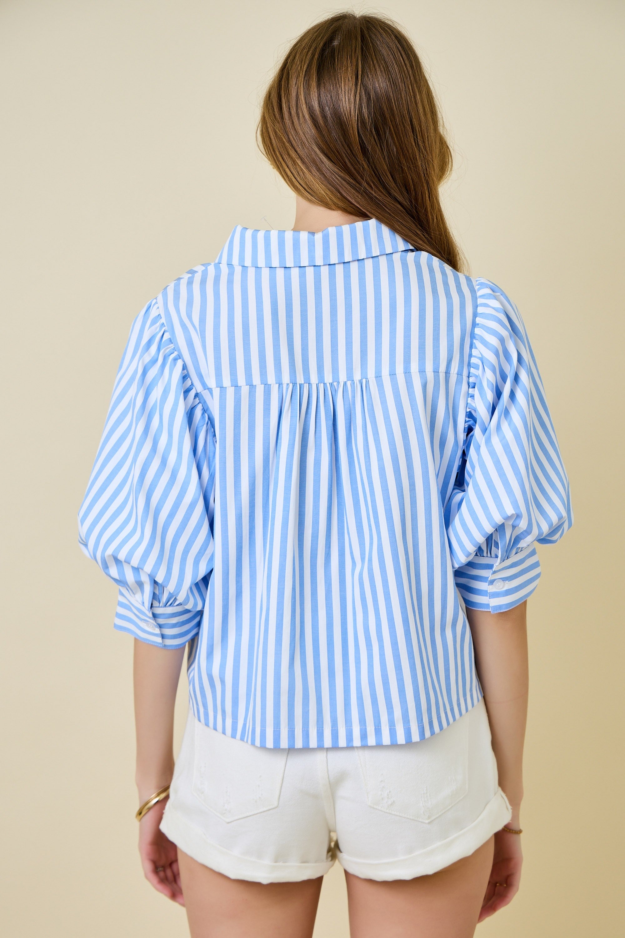 Woman wearing a blue and white striped shirt with balloon sleeves on a beige background