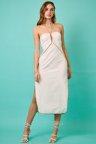 Woman wearing a strapless white dress with a slit on a teal background