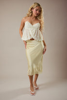 Woman wearing a white lace top and light yellow skirt against a plain background