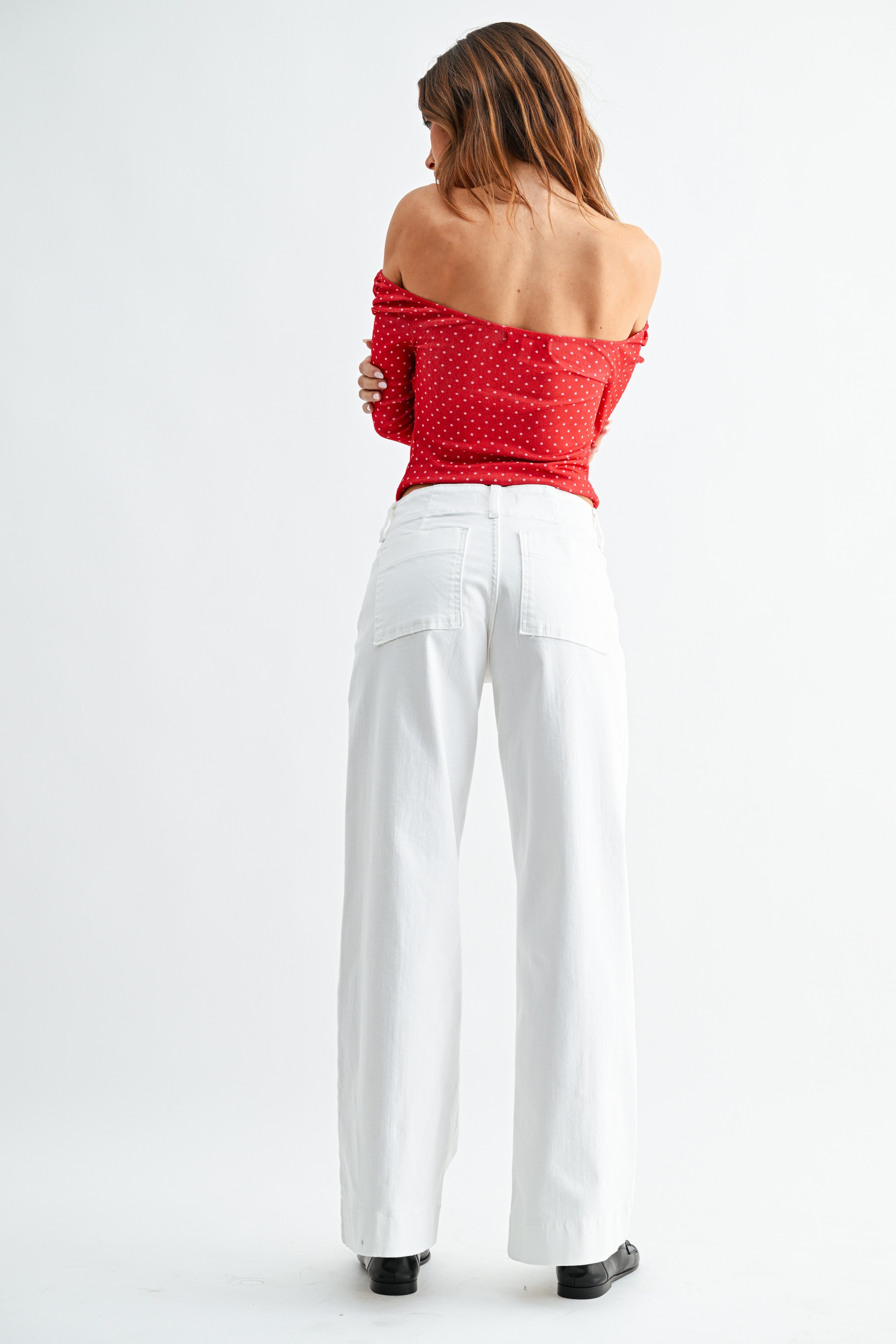 Woman wearing a red off-shoulder top and white pants on a white background