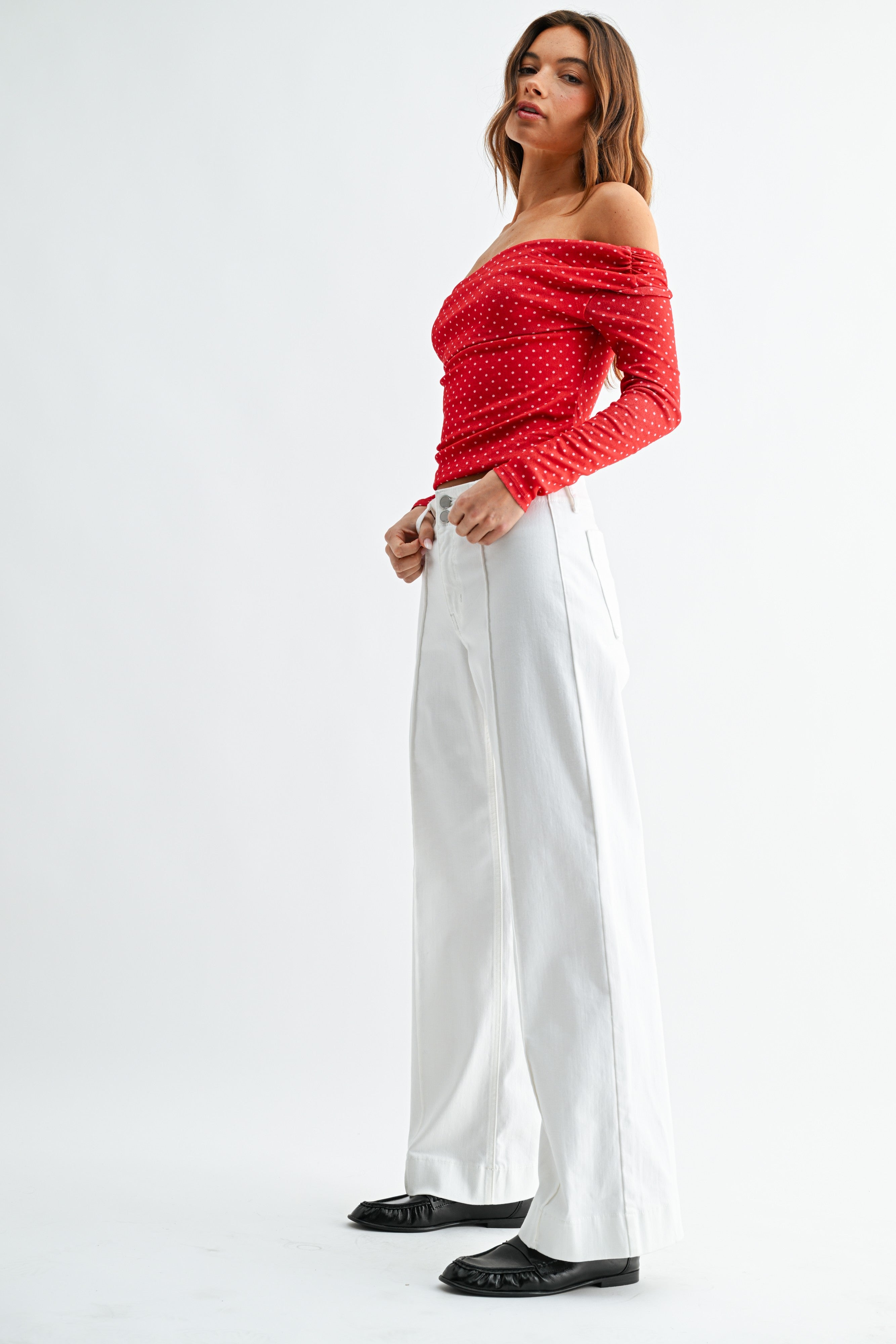 Woman wearing a red off-shoulder top and white pants on a white background