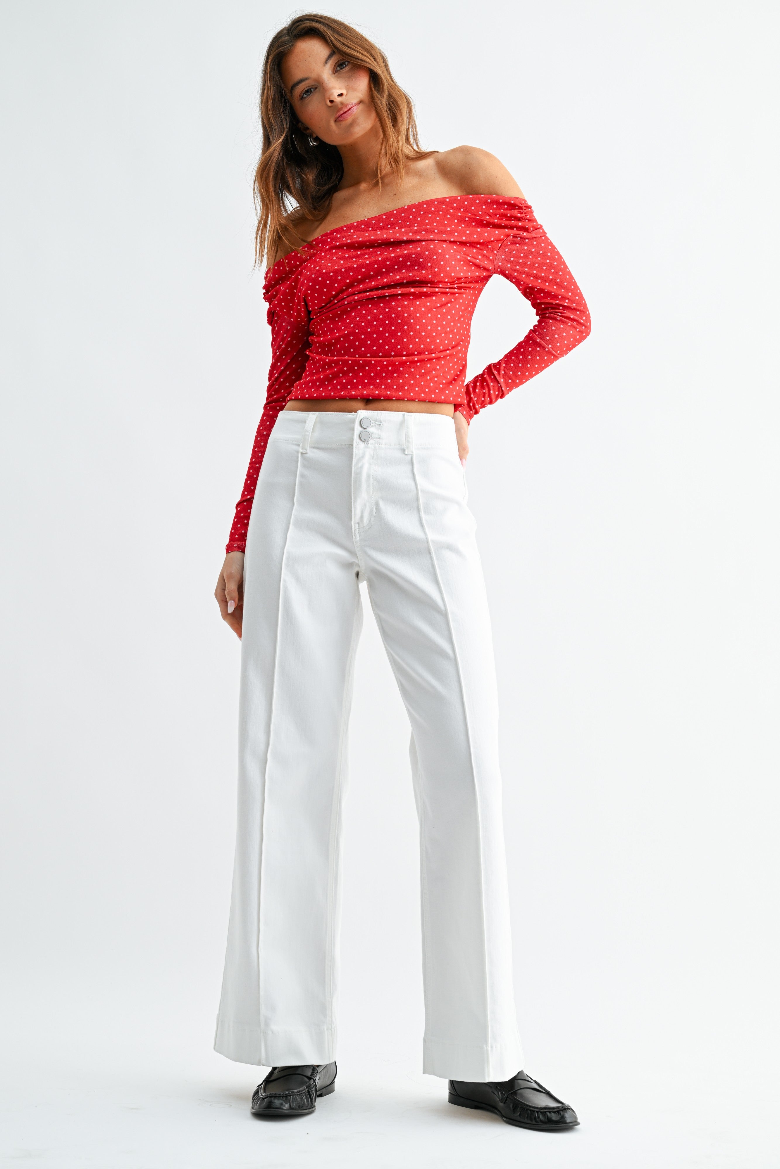 Woman wearing a red off-shoulder top and white pants on a white background