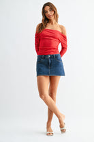 Woman wearing a red off-shoulder top and blue denim skirt on a white background