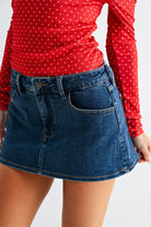 Person wearing a red polka dot shirt and blue denim skirt on a white background