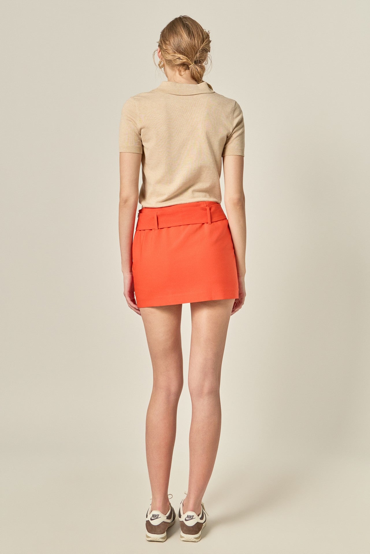 Person wearing a beige polo shirt and orange skirt on a plain background