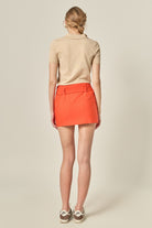 Person wearing a beige polo shirt and orange skirt on a plain background