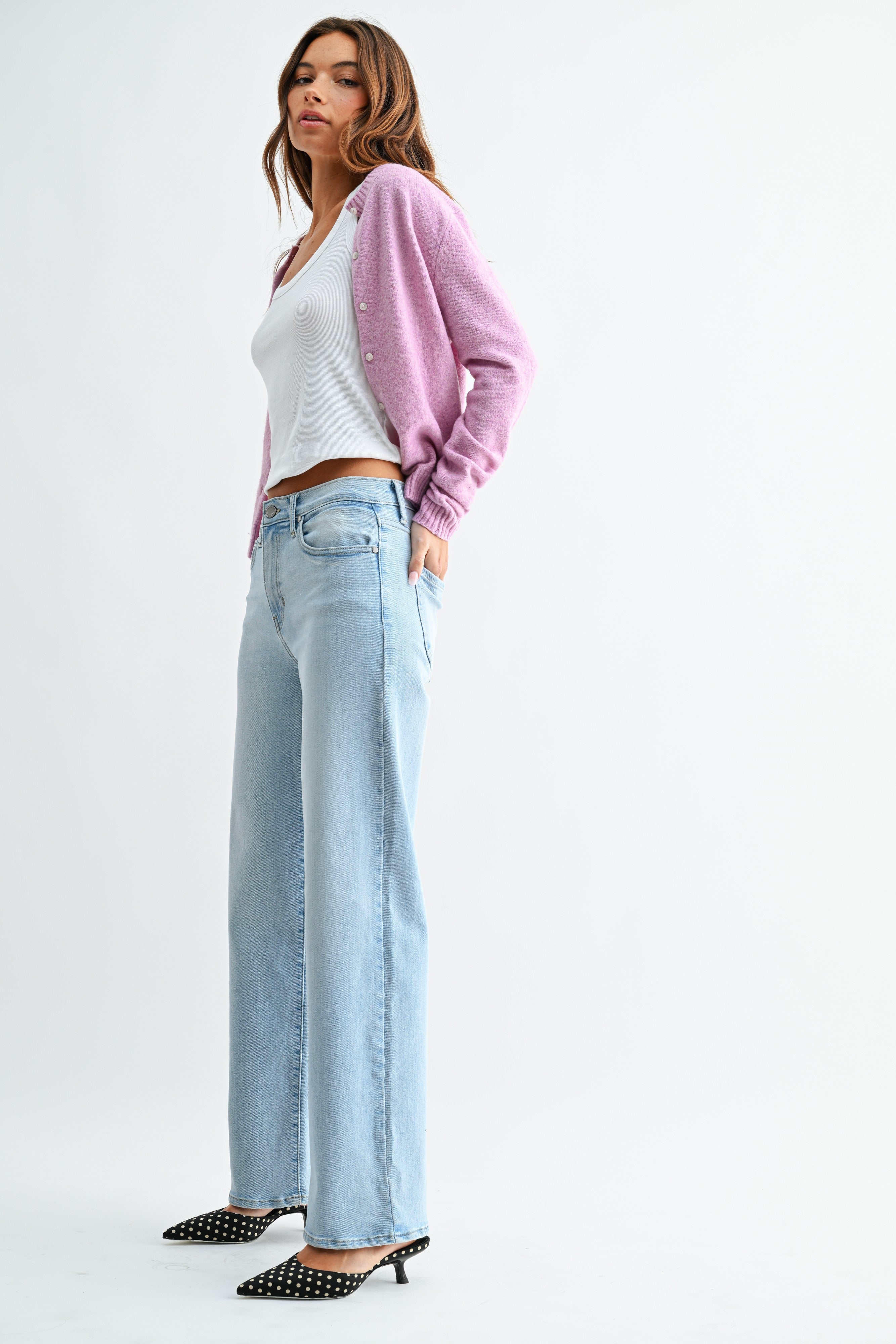Woman wearing a white top, light blue jeans, and a pink cardigan on a white background