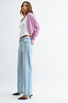 Woman wearing a white top, light blue jeans, and a pink cardigan on a white background