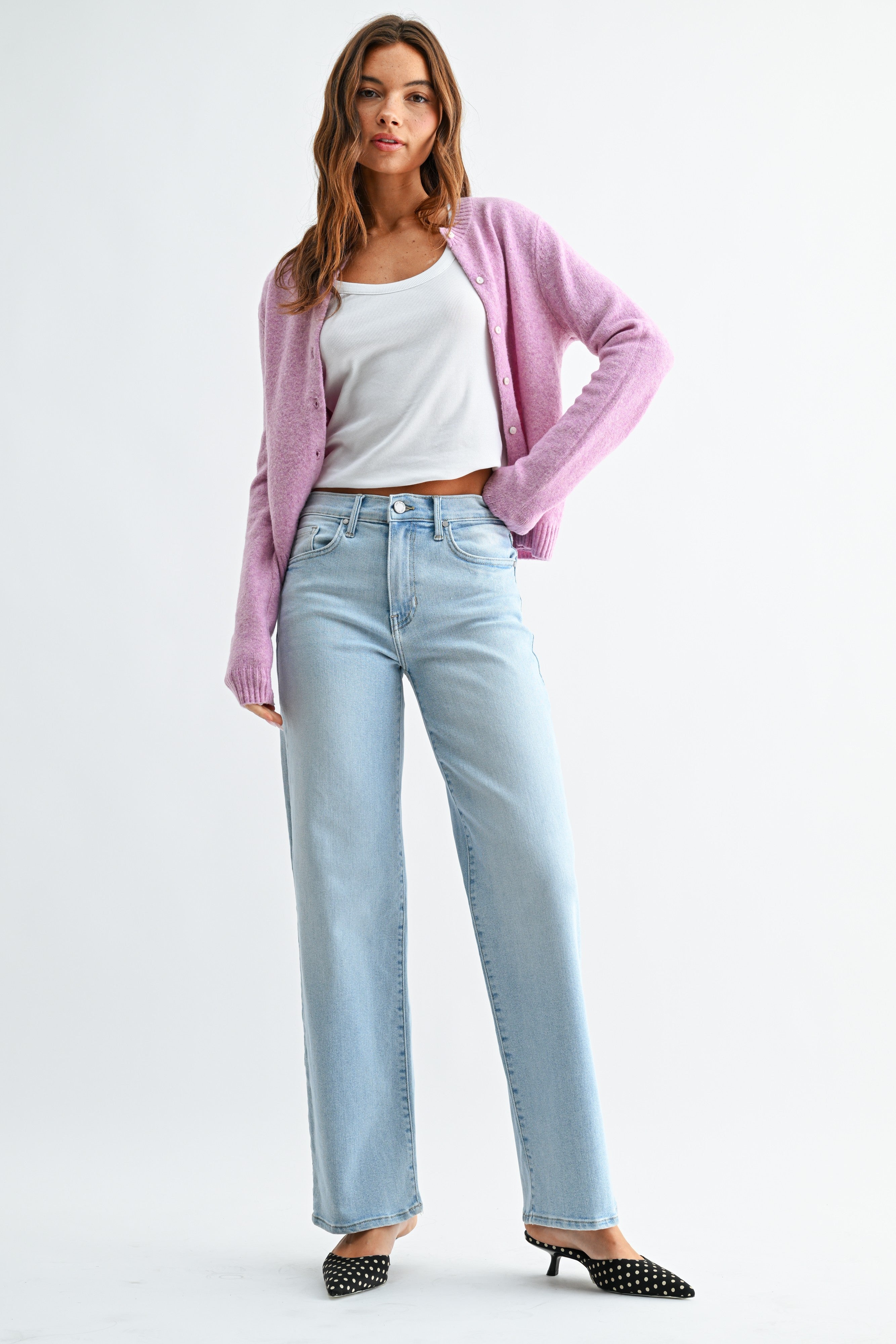 Woman wearing a pink cardigan, white top, and light blue jeans on a white background