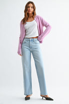 Woman wearing a pink cardigan, white top, and light blue jeans on a white background
