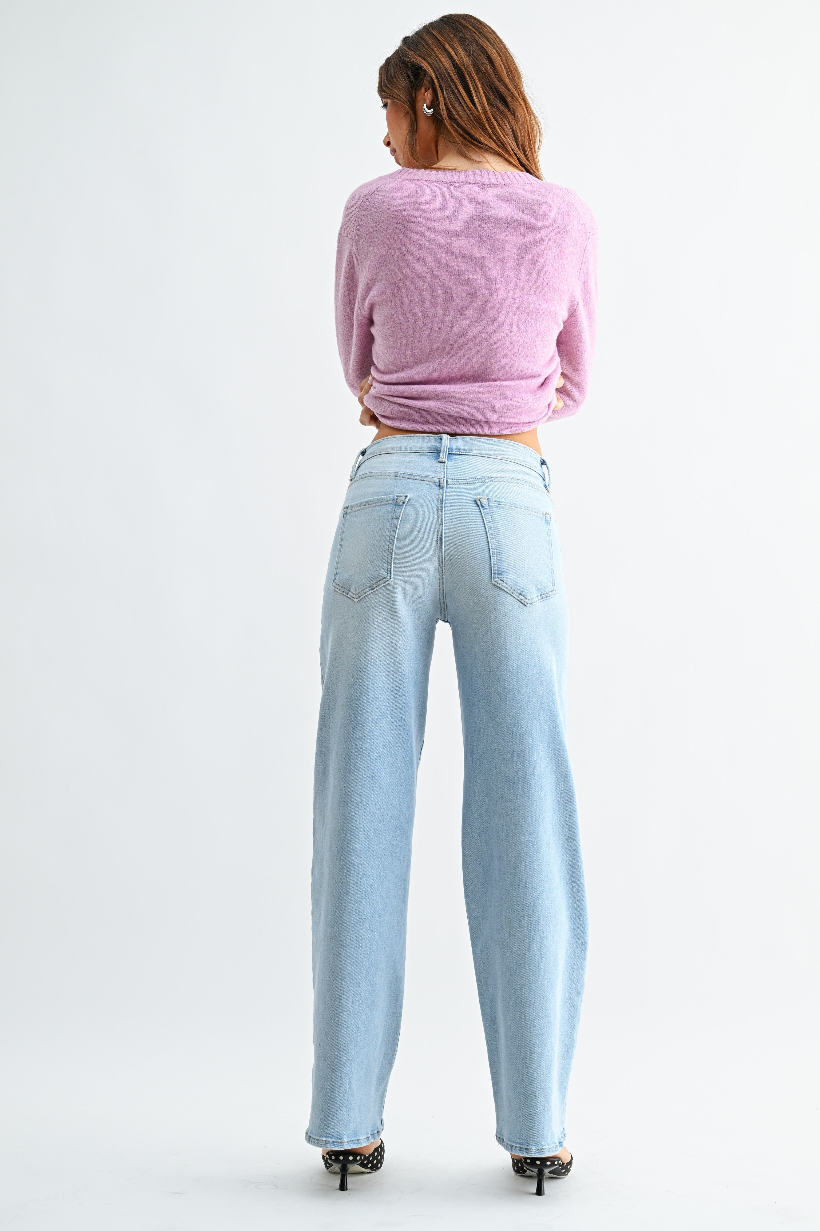 Person wearing light blue jeans and a pink sweater on a white background