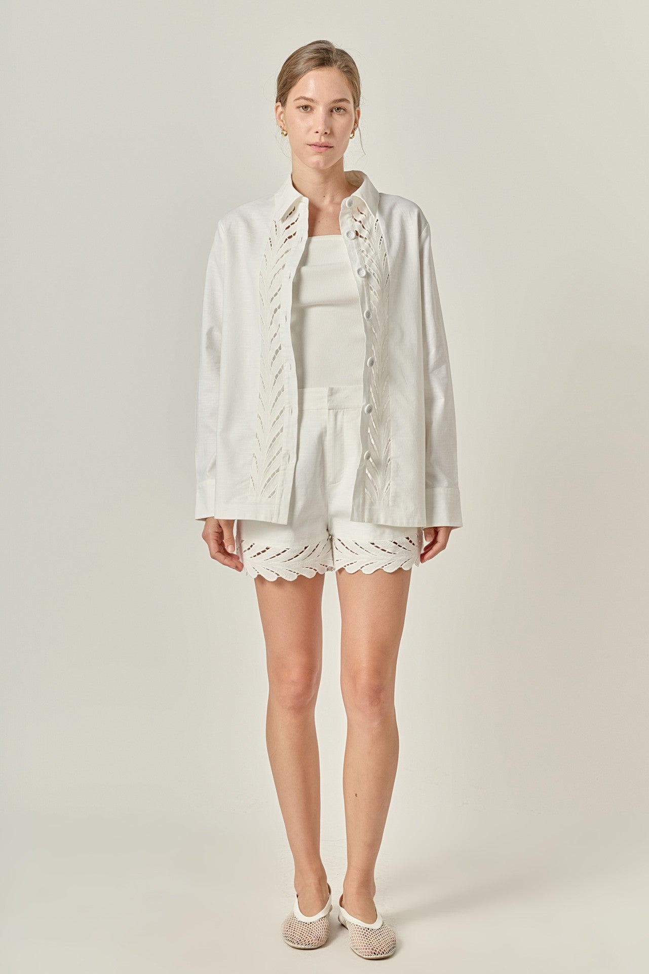 Woman wearing a light-colored outfit with a jacket and shorts on a plain background