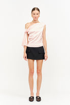 Woman wearing a one-shoulder top with a polka dot pattern and a black skirt on a white background
