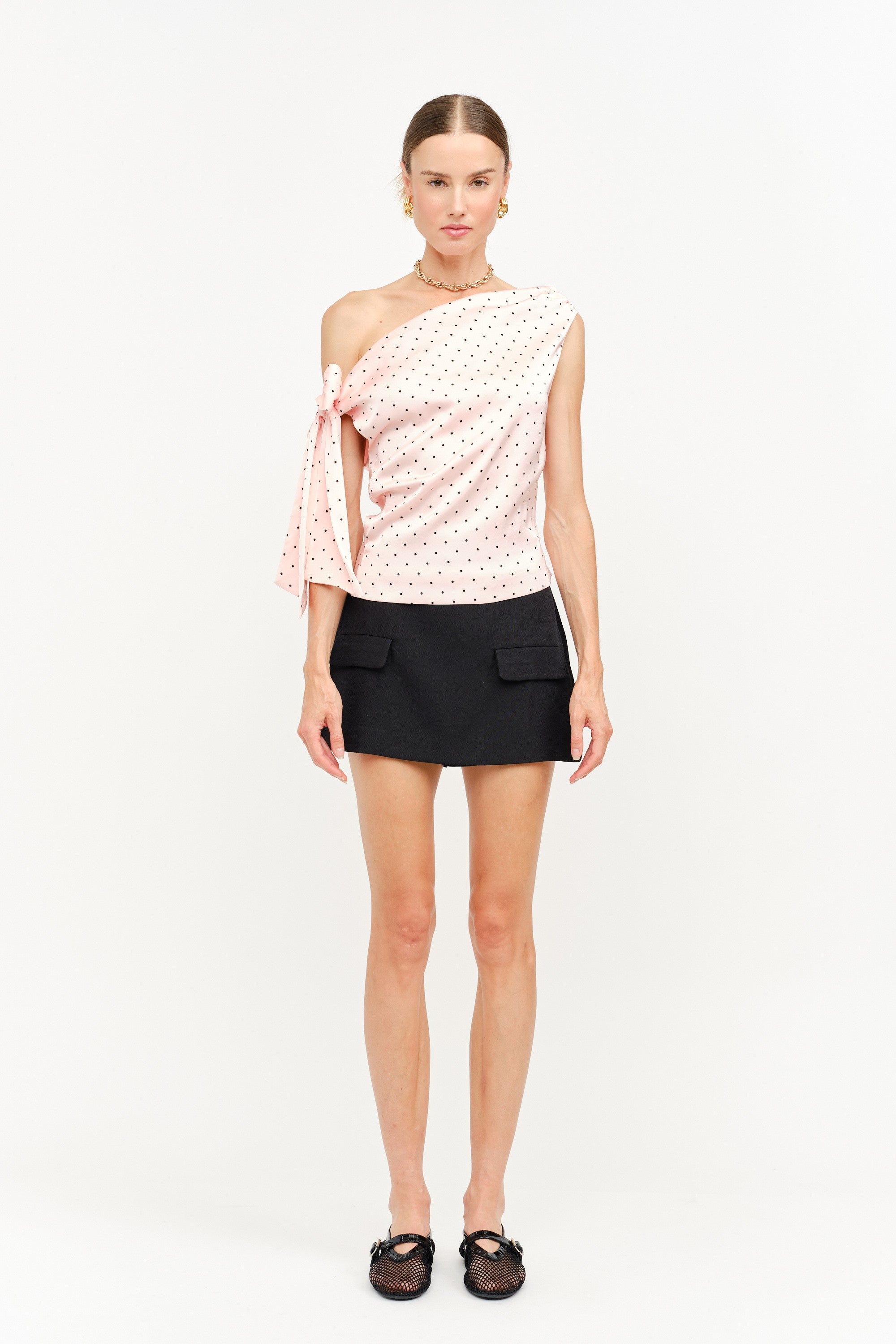 Woman wearing a one-shoulder top with a polka dot pattern and a black skirt on a white background