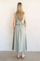 Woman wearing a light green dress standing against a white wall.