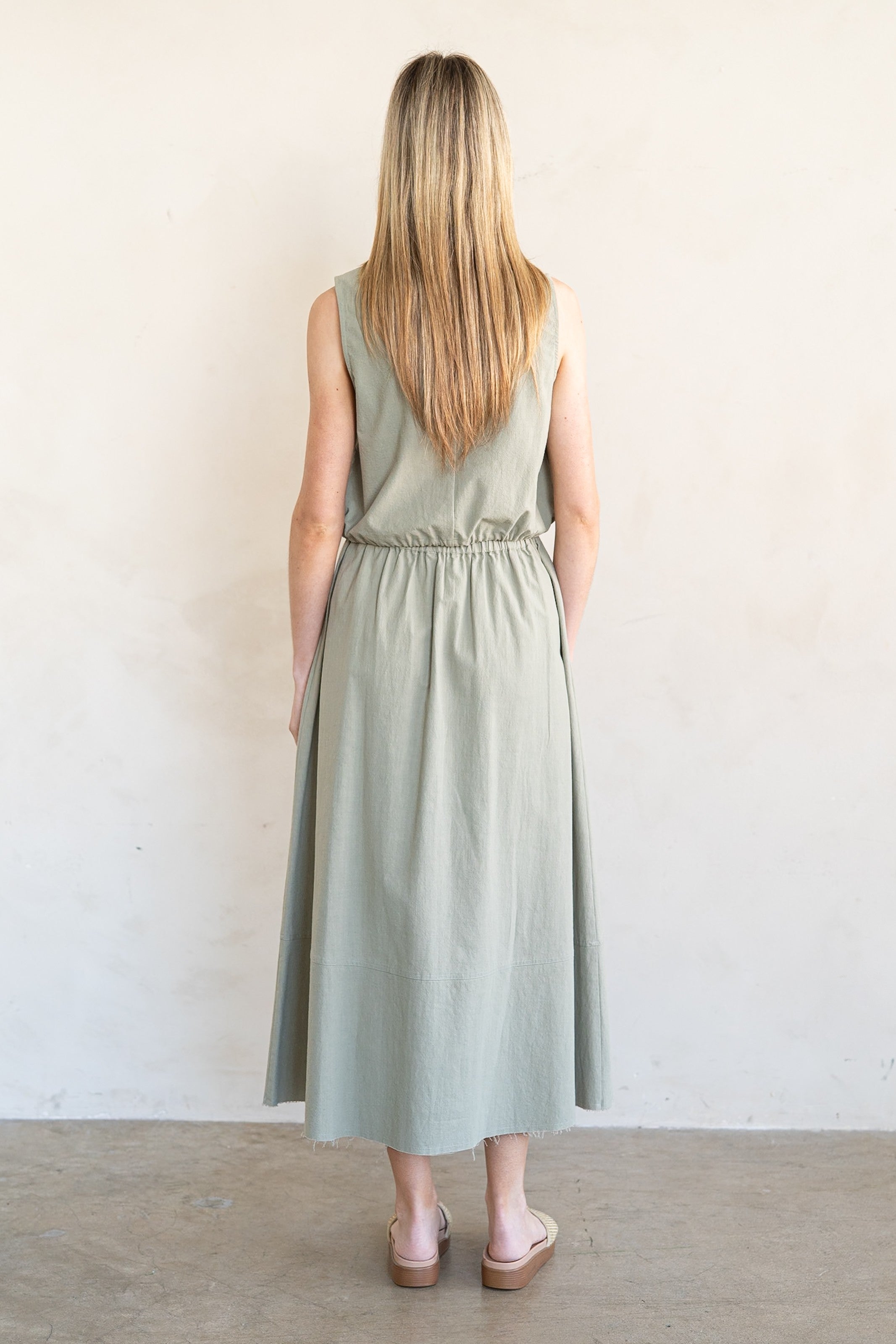 Woman wearing a light green dress standing against a white wall.