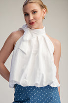 Woman wearing a white blouse with a bow detail on a plain background