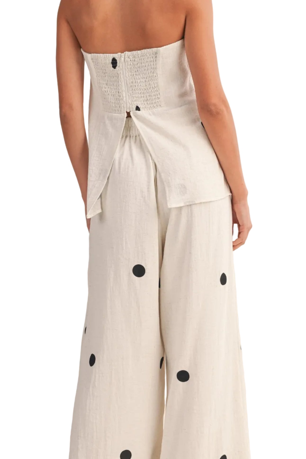 Woman wearing a strapless top and wide-leg pants with black polka dots on a beige background