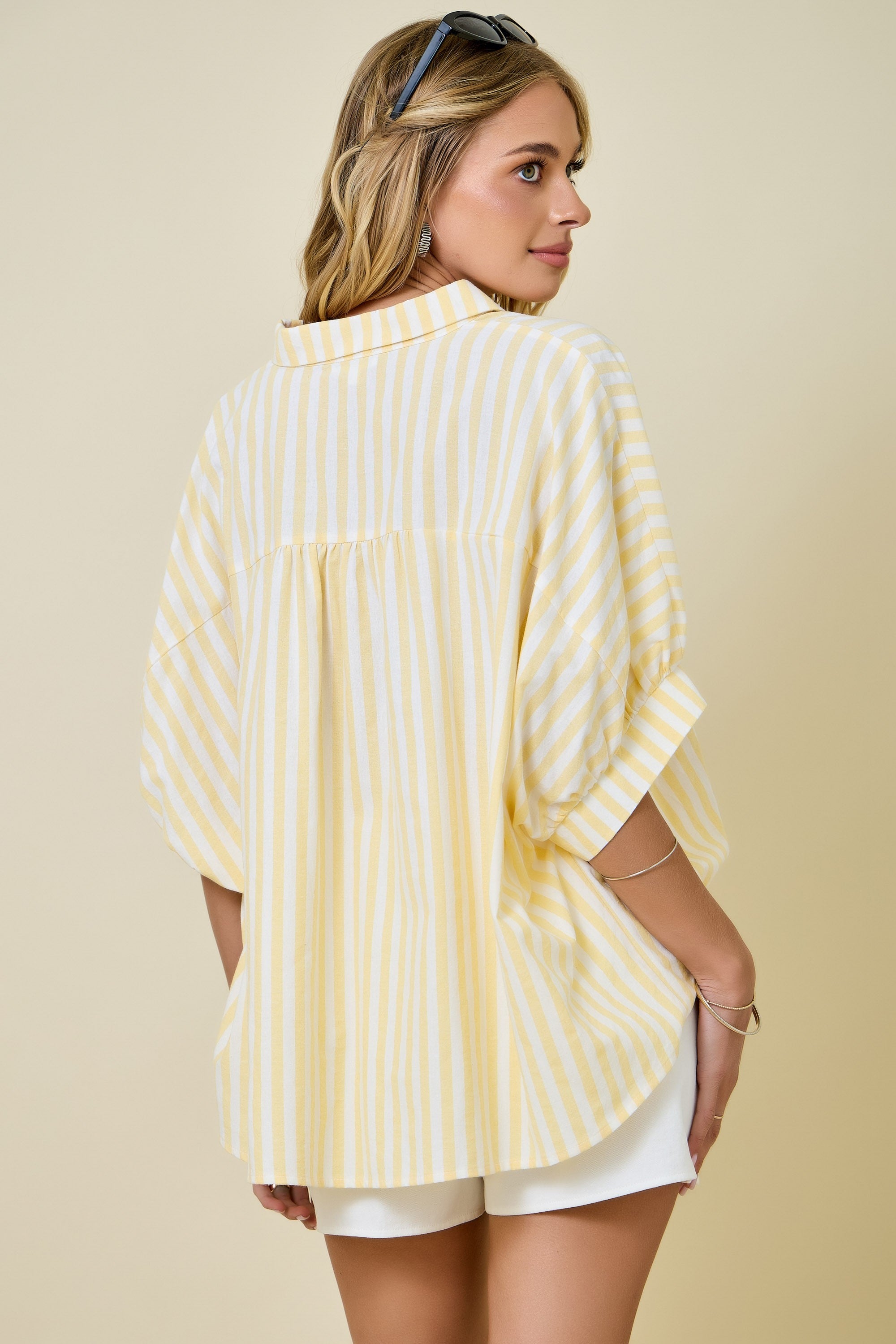 Woman wearing a yellow and white striped shirt and white shorts on a beige background