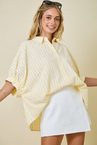 Woman wearing a yellow striped shirt and white shorts against a beige background