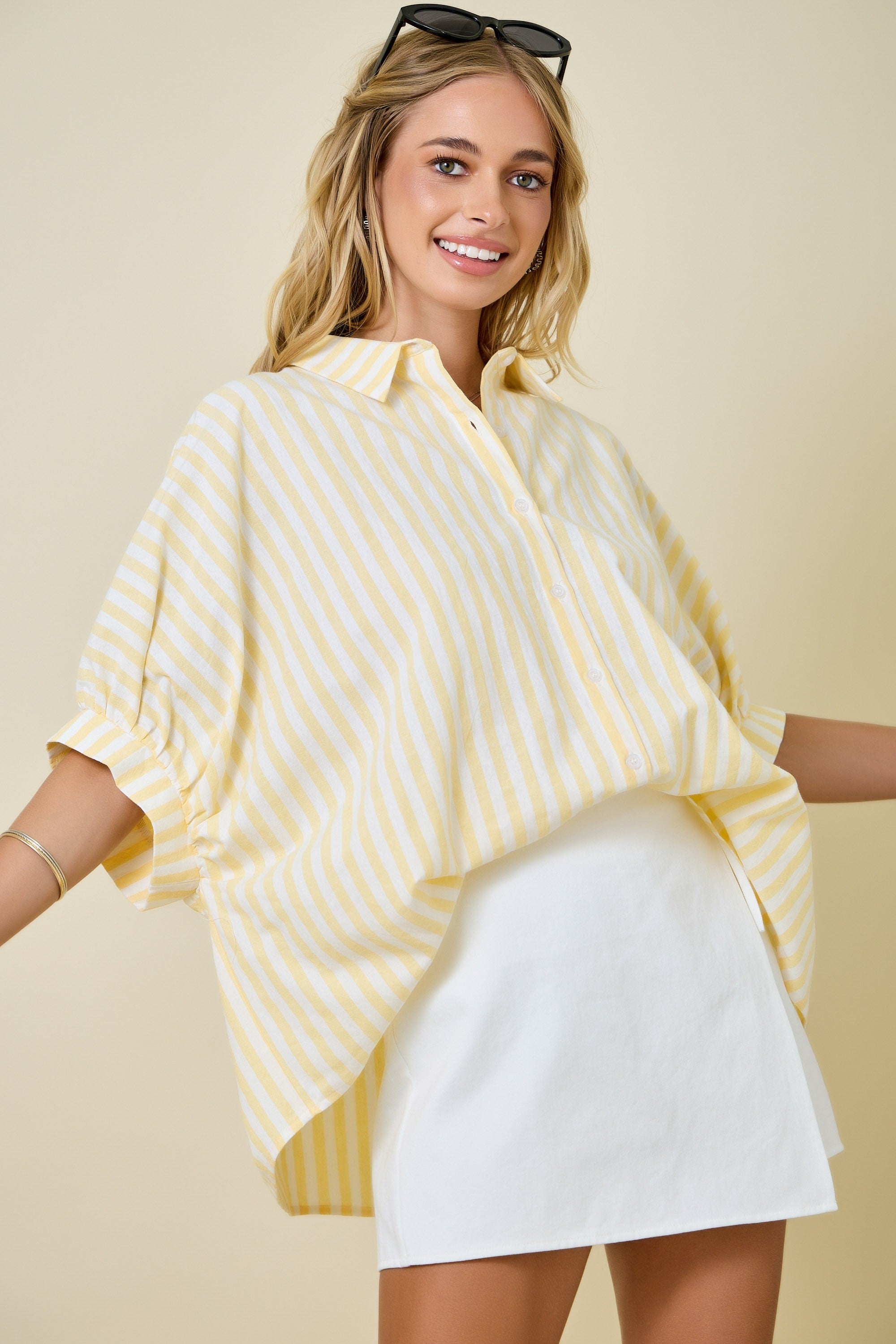 Woman wearing a yellow striped shirt and white shorts against a beige background