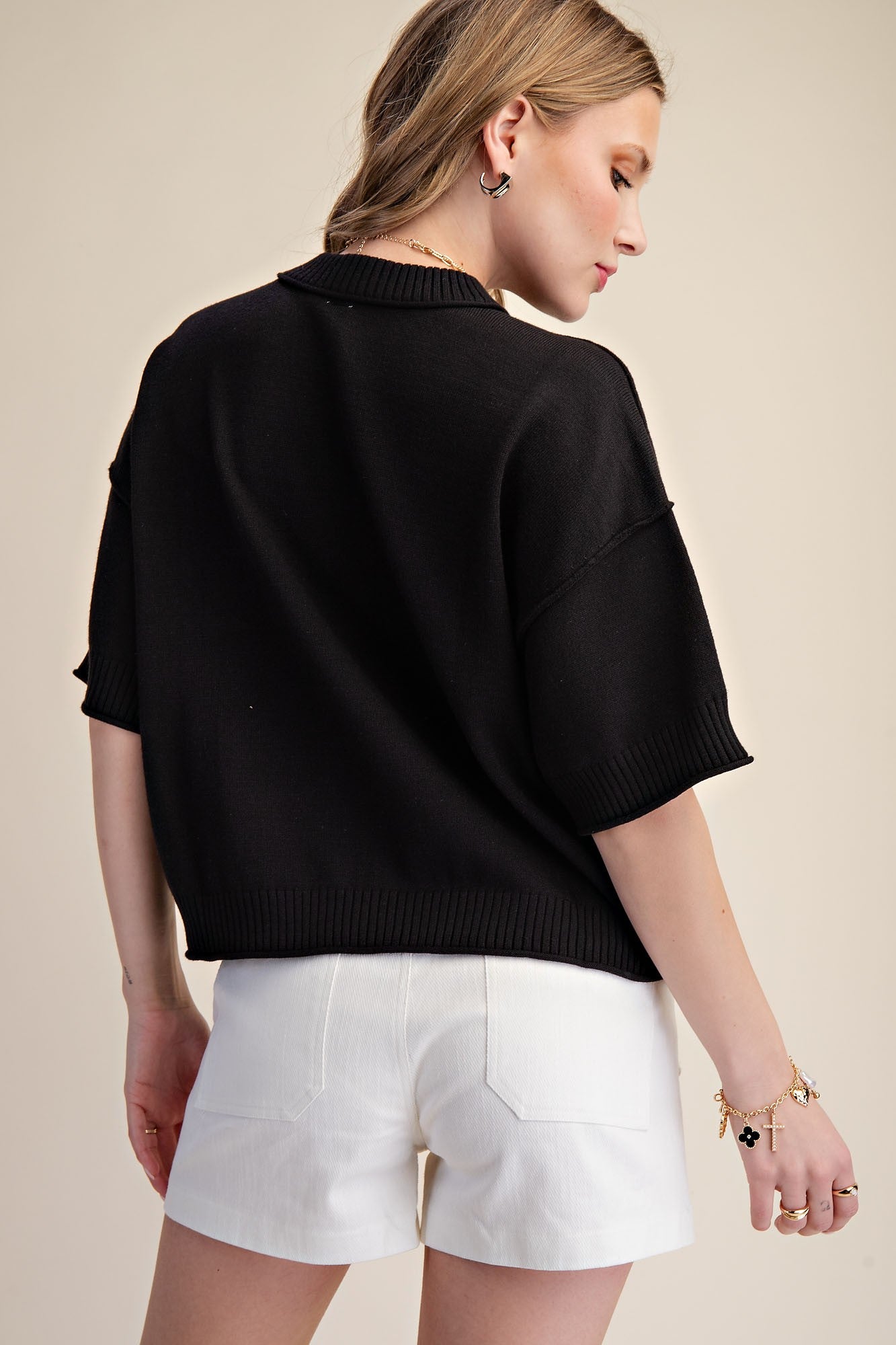 Person wearing a black oversized sweater and white shorts on a beige background