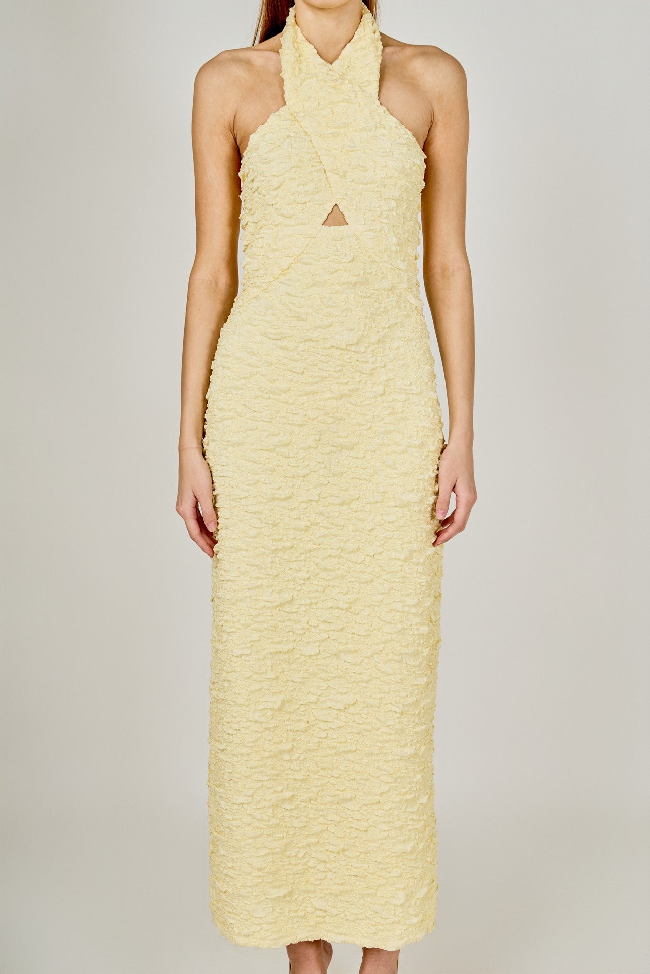 Woman wearing a light yellow halter neck dress on a plain background