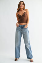 Woman wearing a brown top with embellishments and blue jeans on a white background