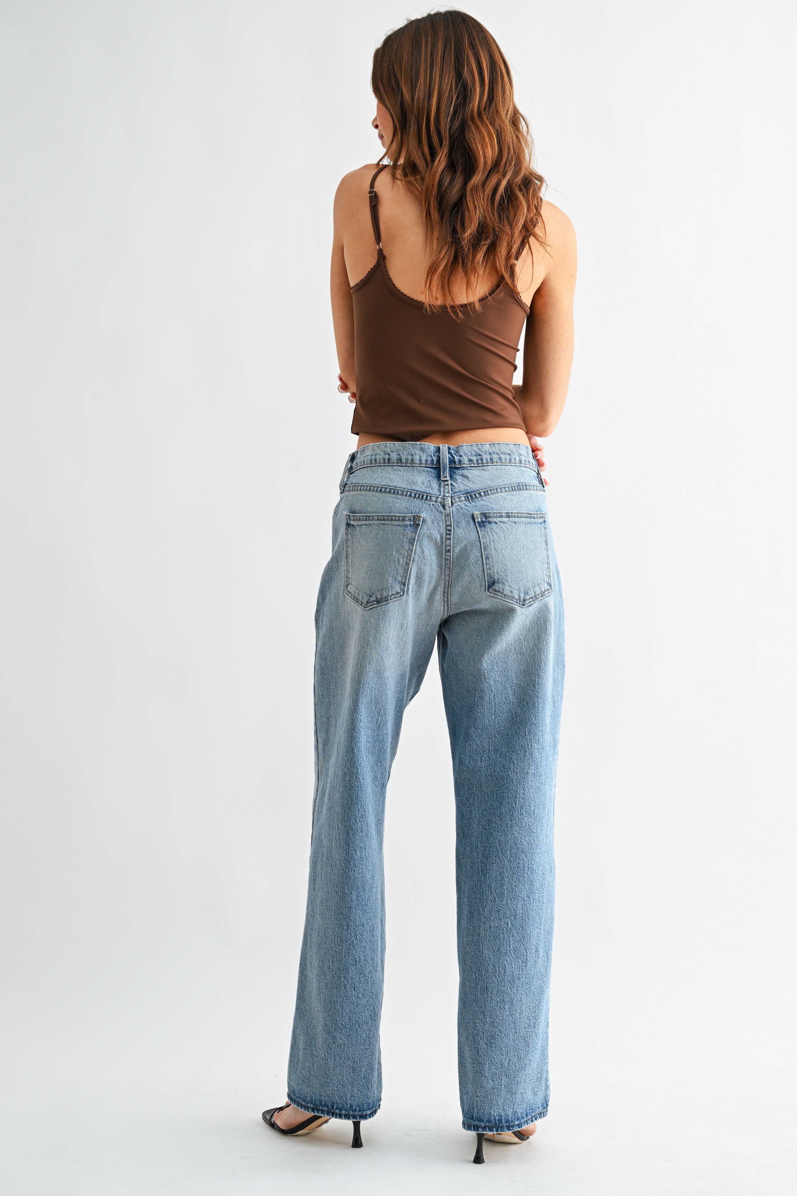 Woman wearing blue jeans and a brown top on a white background