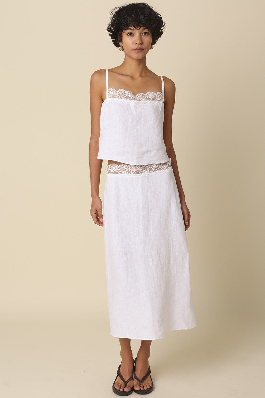 Woman wearing a white top and skirt with lace details on a beige background