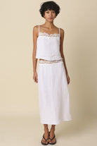 Woman wearing a white top and skirt with lace details on a beige background