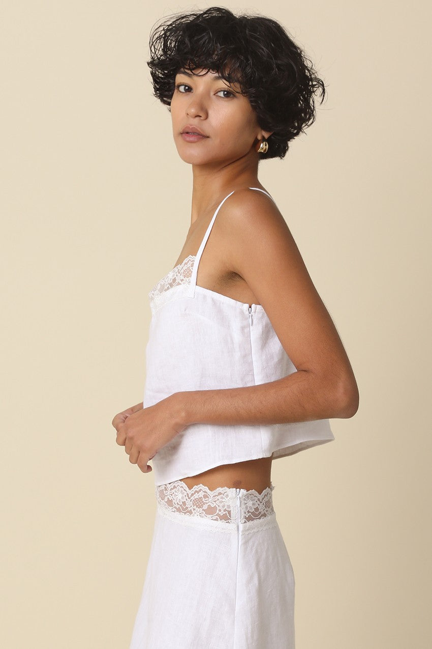 Woman wearing a white lace-trimmed top and pants against a beige background
