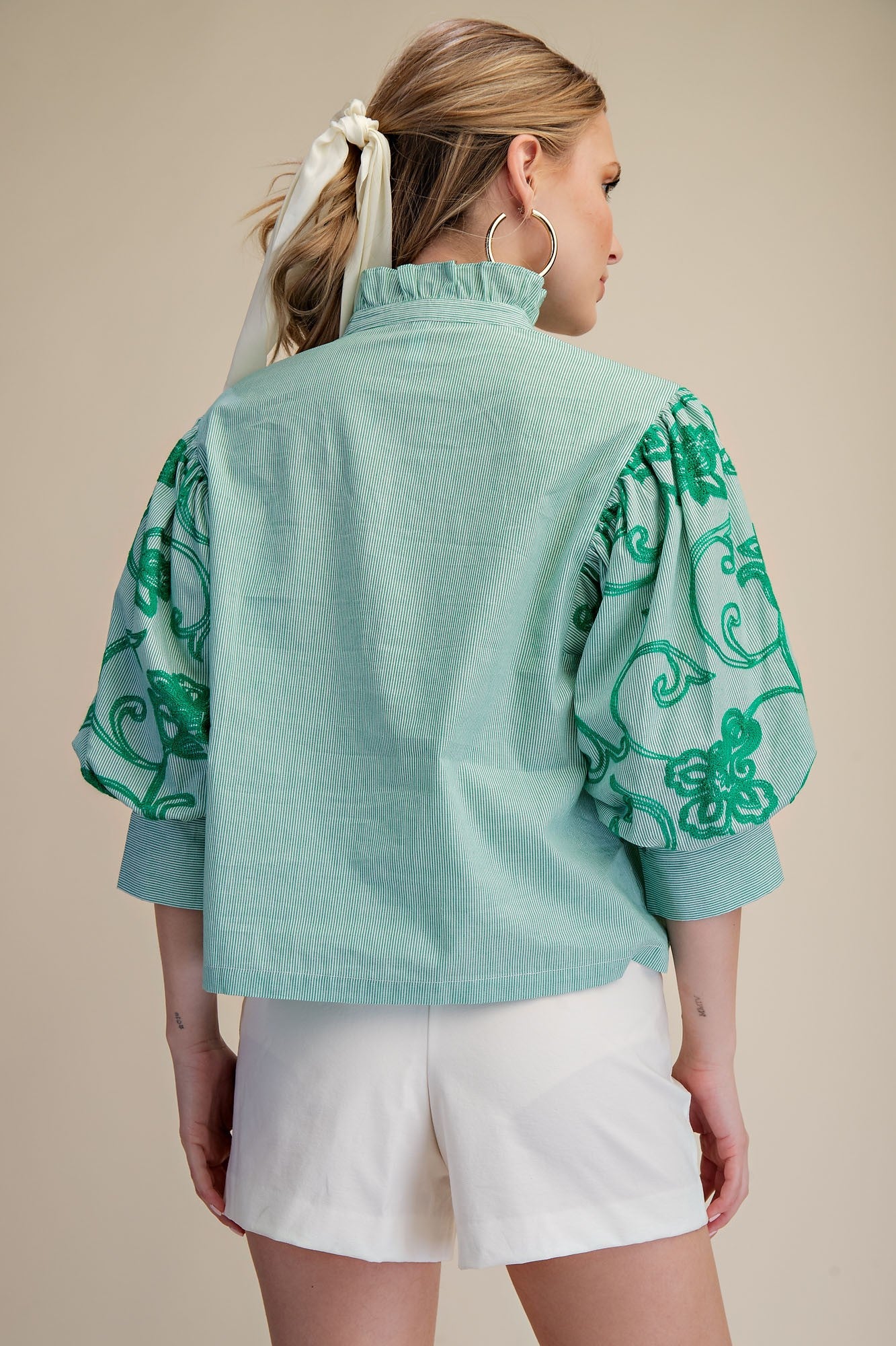 Woman wearing a light blue blouse with green floral patterns on a beige background