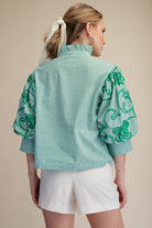 Woman wearing a light blue blouse with green floral patterns on a beige background