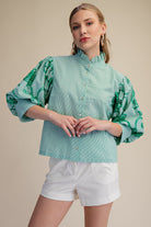Woman wearing a light green blouse with floral patterns and white shorts on a beige background